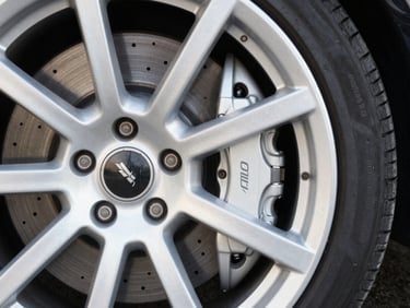 Close-up of a pristine, detailed modern sports car wheel and brake caliper, soft natural daylight, clean dark background