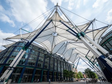 Wide architectural shot of a modern tensile membrane roof over a commercial building, bright natural daylight, crisp structural details, deep navy and emerald accents. Low angle, looking up at the structure.