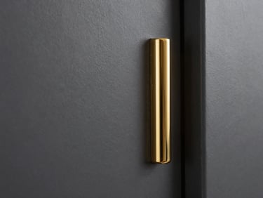 Architectural close-up of a freshly painted matte charcoal wall meeting a polished brass fixture, dramatic side-lighting highlighting the flawless paint texture and sharp gold edge.