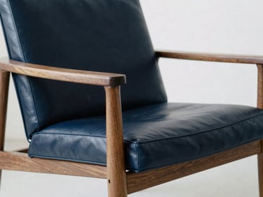 Architectural furniture photography, close-up of a minimalist luxury lounge chair, deep navy leather, warm walnut frame, soft diffused daylight.