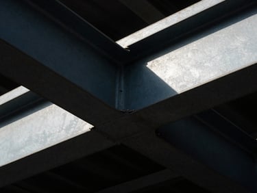 Extreme close-up of heavy steel structural beams with dramatic side-lighting and deep shadows, high-contrast, editorial 35mm film.