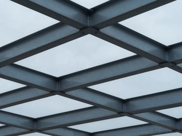 Tight abstract architectural crop of structural steel beams reflecting cool overcast light, desaturated blue tones