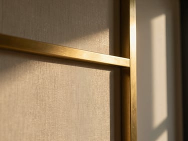 Intimate macro close-up of luxury materials, raw silk wallcoverings meeting solid brushed brass details, soft warm interior shadows.