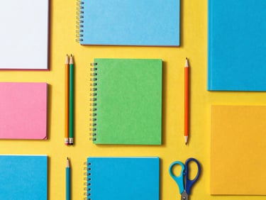 Overhead flat-lay of colorful school supplies, notebooks, pencils, and scissors neatly arranged on a bright yellow surface, high-key natural daylight
