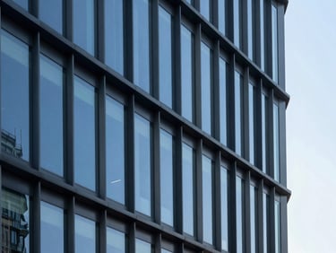 Architectural details of a modern corporate office building, steel and glass facade, sharp angles, cool high-contrast daylight.