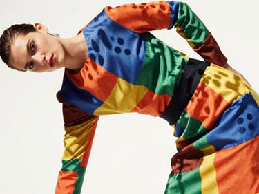 Vibrant editorial photography of a model in a dynamic pose wearing a clashing patterned garment, bright direct midday sunlight casting sharp playful shadows, highly saturated colors, 35mm