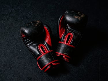 Worn leather boxing gloves resting on a dark canvas floor, sharp red rim light, low-key lighting