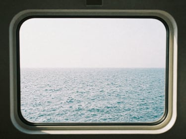 Standard cruise ship cabin window showing realistic grey sea, natural bright daylight, candid 35mm style