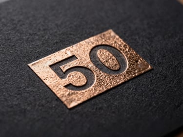 Macro shot of metallic bronze foil stamping embossed on dark paperboard, catching light, sharp edges, high contrast