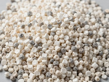 Close-up overhead of HDPE resin granules in natural white and grey tones on a flat industrial surface under studio strobe, granule size uniformity visible, no decorative elements
