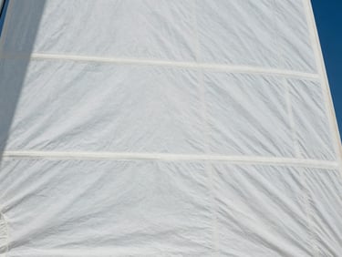 Close-up of white Dacron sail fabric, showing dense weave, light wrinkles, and parallel stitching, minimalist aesthetic