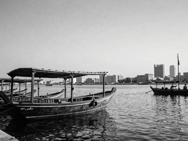 Archival black and white style photograph of historic Dubai Creek with traditional wooden dhows, soft desert light, elegant and respectful framing.