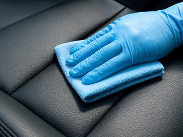 Macro shot of a gloved hand gently wiping a premium black leather car seat with a microfiber cloth, showing a distinct clean versus matte-dirty split.