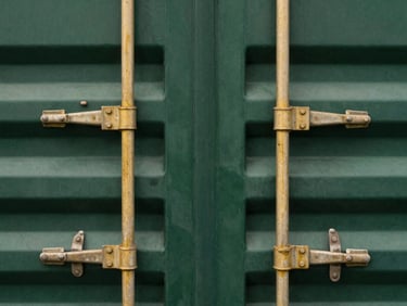 Macro detail of industrial steel shipping container latches, overcast daylight, muted gold and deep green tones