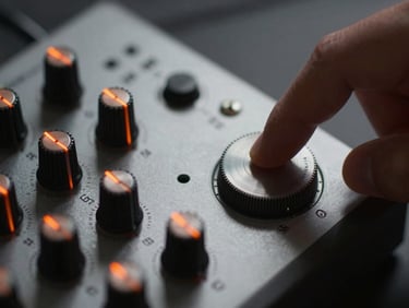 Macro photograph of a finger rotating a physical dial on a custom synthesizer module, low-key lighting with safety orange accents reflecting off the metal hardware.
