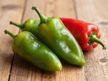 Fresh green and red ají dulce peppers on a rustic wooden surface, warm side lighting