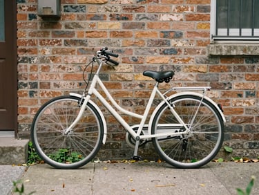 A clean, modern bicycle leaning against a brick wall in a leafy neighborhood courtyard, soft daylight