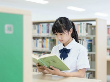 A high school student in uniform reading a book in a bright, modern library, soft focus, emerald green accents, 35mm