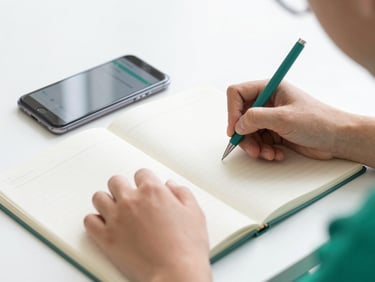 Hands of a student neatly taking notes in a modern notebook next to a smartphone displaying a clean digital dashboard, bright daylight, shallow depth of field