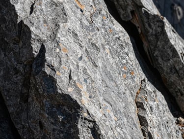 Tactile close-up of honed grey stone and charred timber under harsh high-altitude mountain sunlight casting deep dramatic shadows