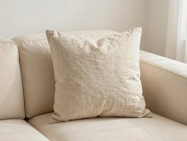 Hands arranging a beige linen pillow on a modern cream sofa, soft natural light, cozy and inviting atmosphere, warm editorial photography, 35mm lens