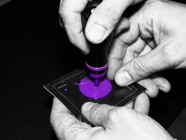 Close-up of hands stamping a dark ticket with purple ink, high-contrast black and white