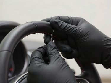 Macro shot of professional hands in black nitrile gloves carefully detailing the leather stitching of a steering wheel, soft focused background, clean studio lighting.
