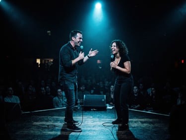 Wide-angle dramatic stage shot of two stand-up comedians under a single electric neon-blue spotlight, deep ink shadows, grainy 35mm film style.