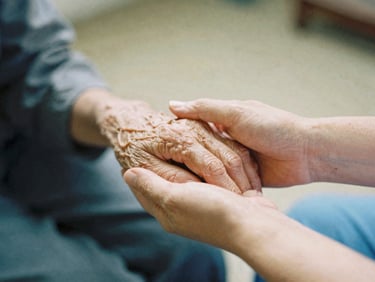 A close-up of a nurse's hands gently holding an elderly patient's hand, soft natural daylight, warm editorial film photography, 35mm.