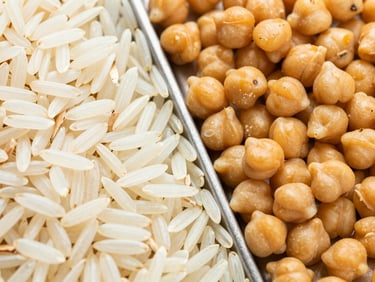 Macro overhead flat-lay of long-grain basmati rice and golden chickpeas divided by a clean metal edge, bright natural daylight, high texture detail