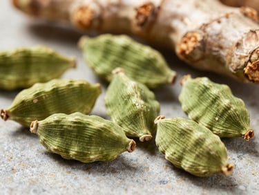 Macro close-up of vibrant whole green cardamom pods and raw turmeric roots on a neutral stone surface, high texture detail.
