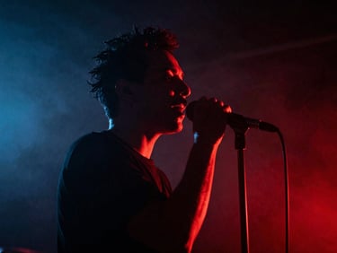 Close-up de um cantor performando em um palco com iluminação dramática vermelha e azul, fumaça, fotografia cinematográfica, alto contraste.