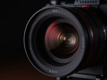 Close-up of a high-end cinema camera lens with dramatic chiaroscuro lighting, subtle red reflections, anamorphic lens flare, cinematic film photography, deep blacks, studio environment.