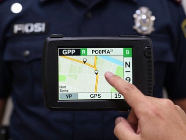 Close-up of a GPS device screen showing a patrol route, with a uniformed hand pointing, sharp daylight, deep navy and amber tones, high contrast, 35mm lens