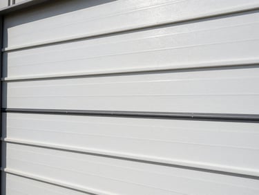 Close-up of a high-density insulated steel garage door panel showing weather-stripping seals, bright daylight