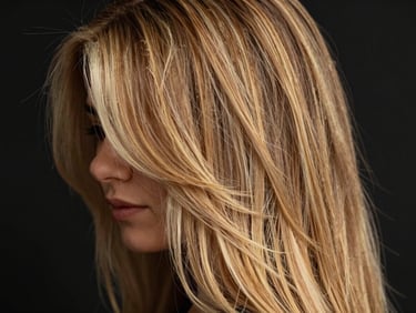 Close-up of a woman's hair, showcasing multi-dimensional premium blonde highlights with natural root blend, warm studio lighting, rich black background, shallow depth of field, 85mm lens