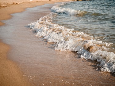 Close-up environmental shot of waves breaking on a sandy beach in Agadir, warm morning light, soft shadows, shallow depth of field, 35mm film