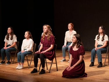 A local Indiana family actor group rehearsing under warm spotlight beams, wooden floorboards visible, authentic candid expressions