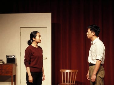 Candid medium shot of two community actors rehearsing a scene on a local stage, warm low-key spotlighting, vintage props, 35mm film grain