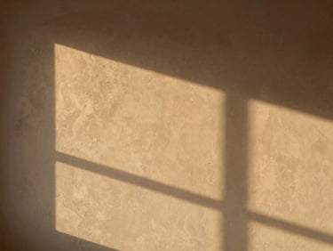 Wide environmental interior shot of a finished wall with clayxible texture, warm golden-hour light raking across the surface revealing subtle depth and tone variation, no people, no furniture clutter