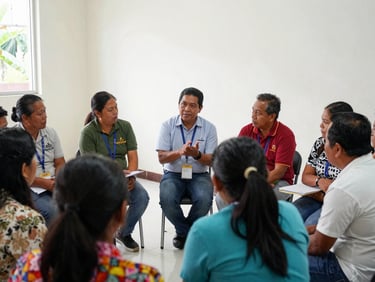 A small group of Bicolano community members attending a workshop, engaging with a GMVCC faculty member, bright indoor lighting, focused discussion.