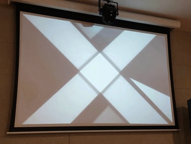 Sharp gobo projection of a geometric pattern on a textured venue wall, spot fixture visible at upper frame, daylight-balanced venue interior surrounding the projection, functional and precise