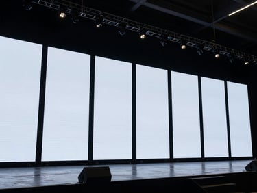 Wide shot of an indoor LED video wall displaying live presentation content on a fully rigged stage, no audience visible, taken from front of house angle showing the complete panel structure and bright even illumination, technical setup visible