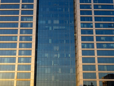 Symmetrical architectural shot of a modern glass and steel commercial skyscraper facade in Riyadh, reflecting the golden hour sky, clean lines, sharp focus, 35mm lens.