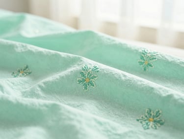 A close-up of premium mint green cotton fabric with delicate hand-stitched floral embroidery, soft natural window light, shallow depth of field.
