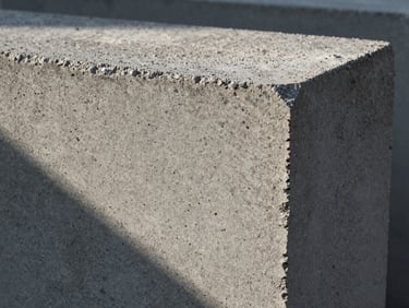 Macro texture of a solid concrete block showing dense aggregate composition, deep shadows cast by high-contrast early morning light.