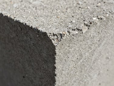 Macro close-up of a concrete block's dense, rough aggregate texture under harsh sunlight, emphasizing structural integrity and raw material quality.