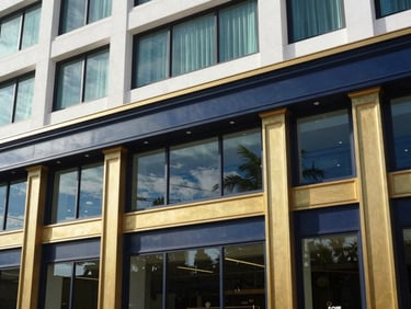 Architectural detail of a premium commercial building facade in South Florida, bright natural coastal window light, deep navy and warm gold accents, sharp focus, 35mm lens
