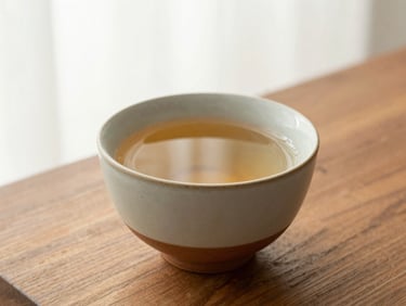 A close-up of a ceramic cup with herbal tea on a wooden table, soft morning window light