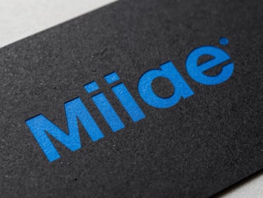 Macro crop of physical brand collateral, heavy black paper stock with debossed electric blue typography, hard studio key light, sharp angles